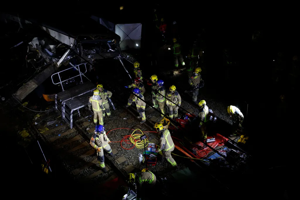 Firefighters investigating a train crash with a collapsed wall at night.