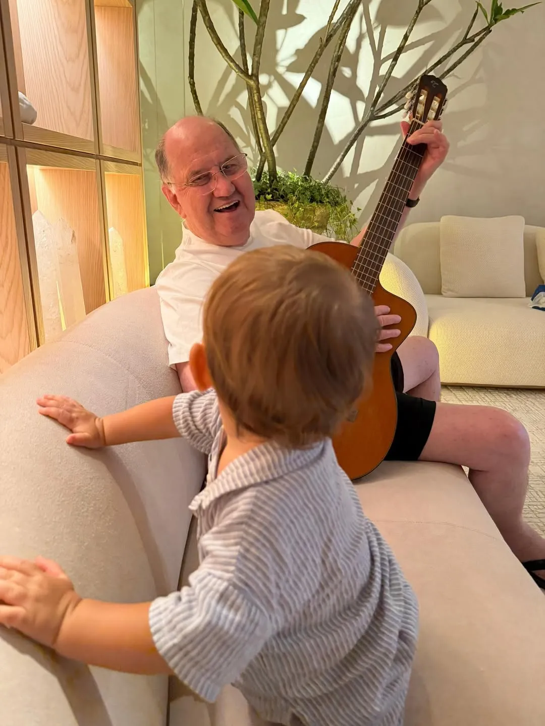 A grandfather playing guitar for a young child.