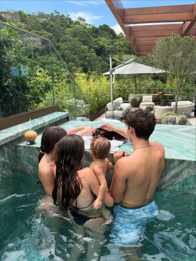 Three children and a baby in a pool, seen from behind.
