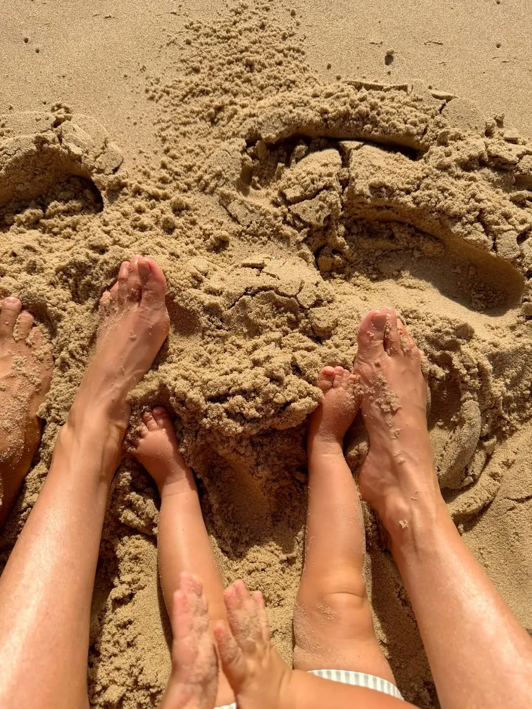 Feet and legs of two adults and two children in the sand.