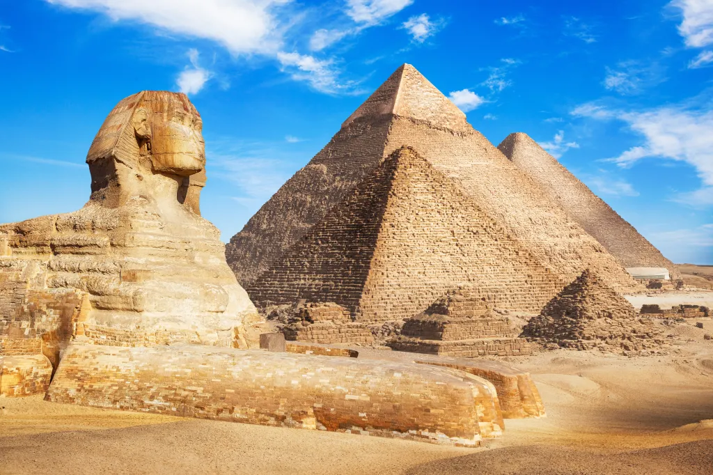 The Great Sphinx of Giza and three pyramids under a bright blue sky with white clouds.