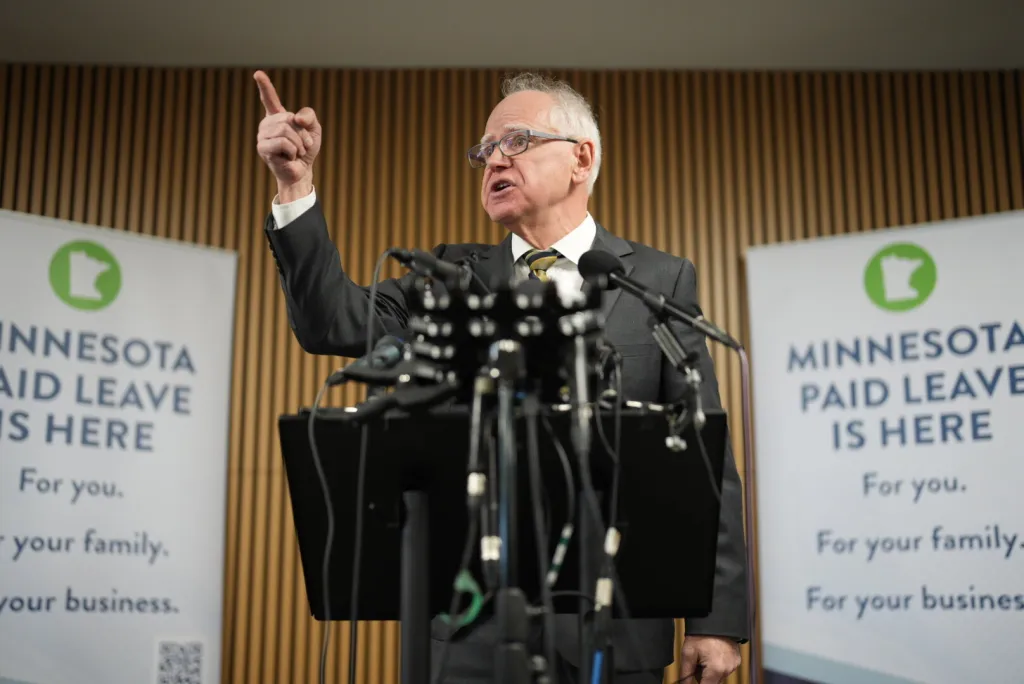 Gov. Tim Walz speaking at a news conference, with banners behind him saying