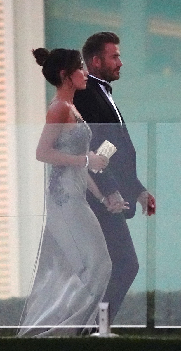 Victoria Beckham in a silver-grey slip dress and David Beckham in a tuxedo, holding hands at Brooklyn's wedding.