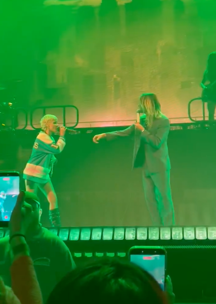 Halsey and Adam Lazzara performing on stage, bathed in green light, with audience members holding up phones to record.