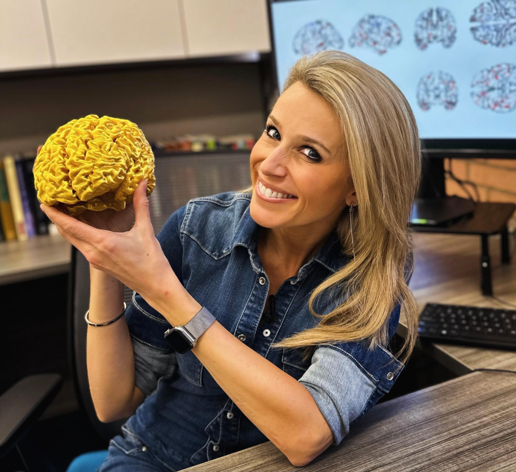 Lara Lewington, author of Hacking Humanity, holding a gold 3D-printed model of her brain.