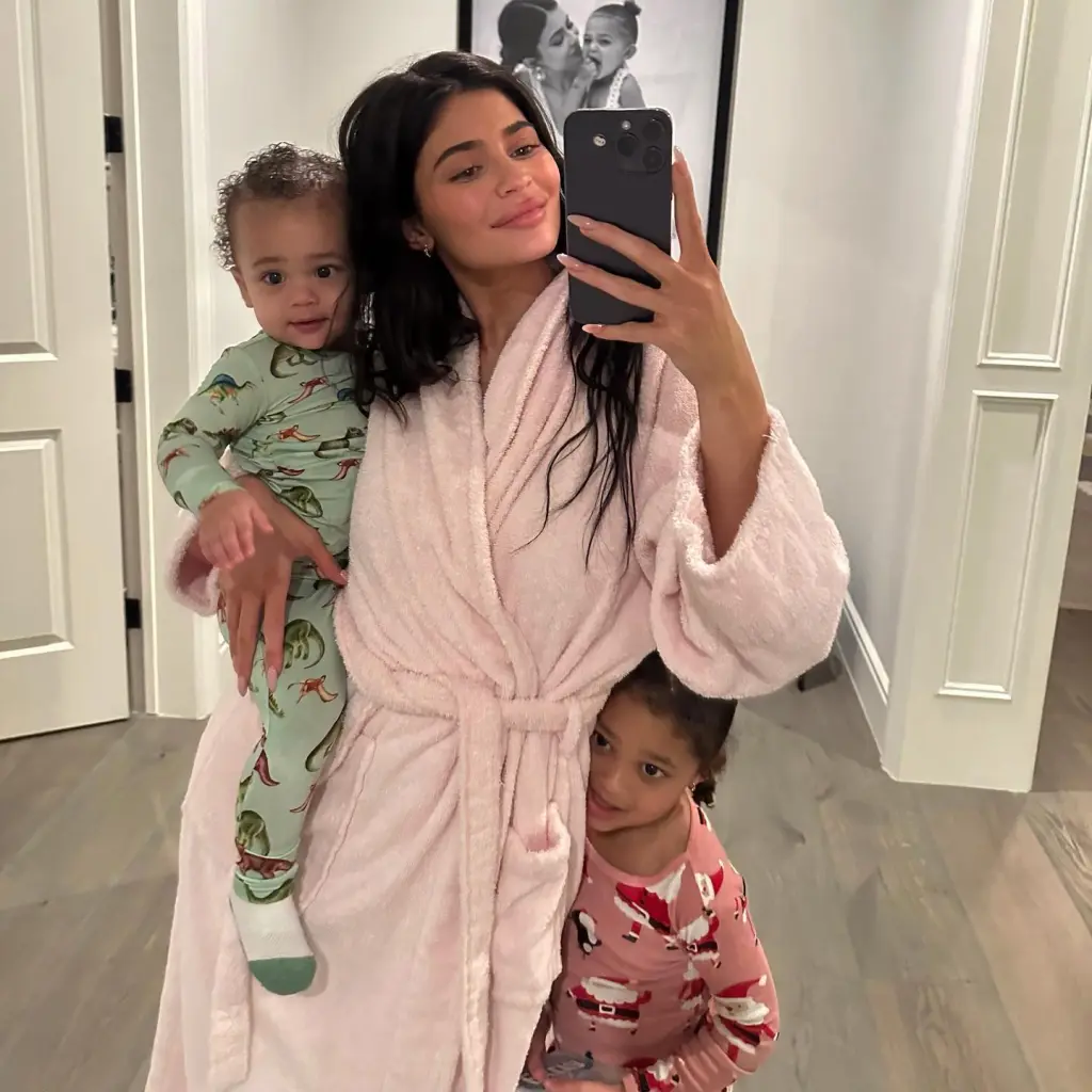 Kylie Jenner takes a mirror selfie while holding her son Aire and her daughter Stormi peeks from behind her.