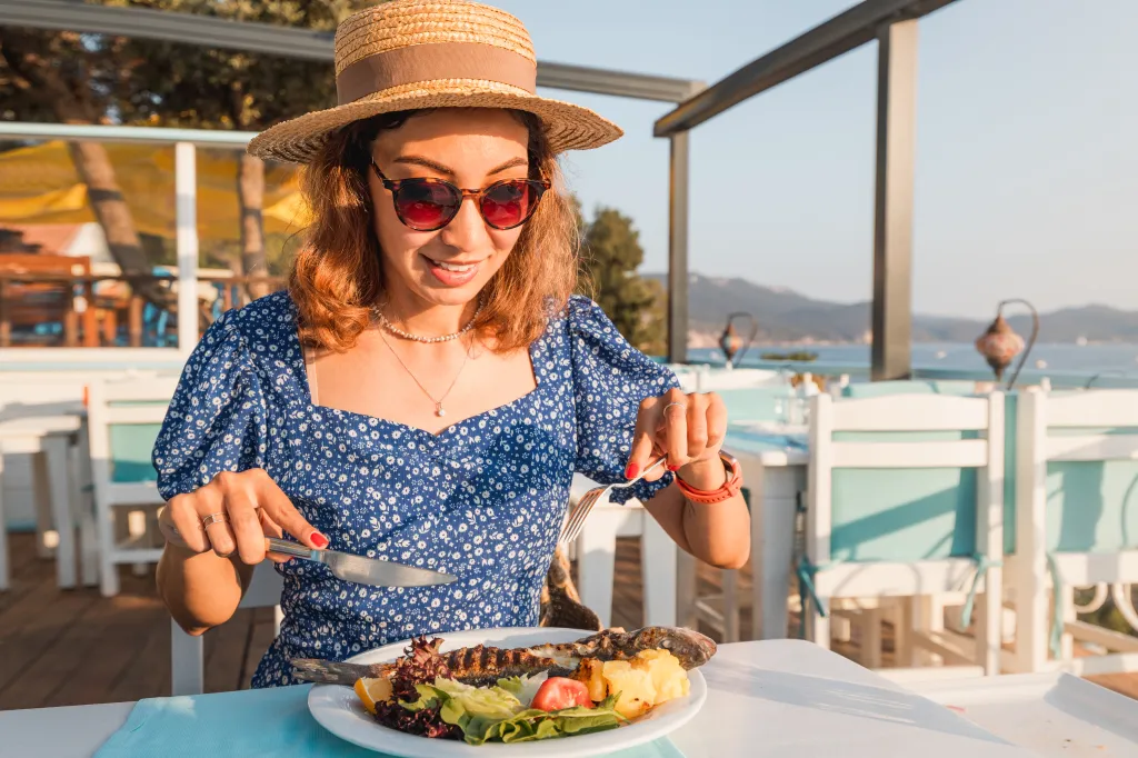 Happy woman eating a baked whole sea bass at an outdoor restaurant.