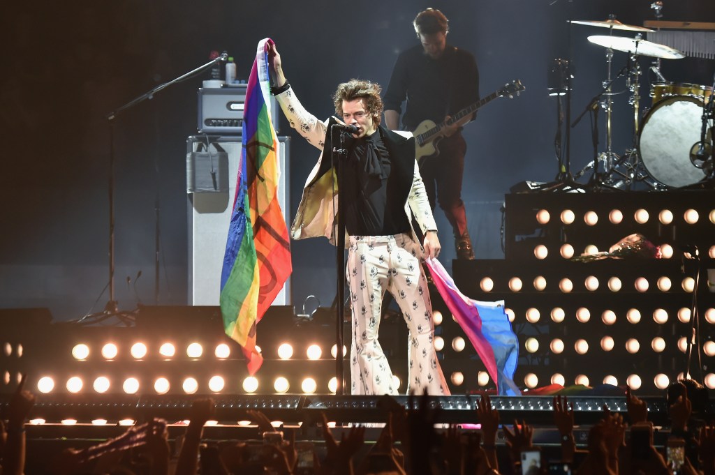 Harry Styles holding rainbow and bisexual pride flags during a concert.