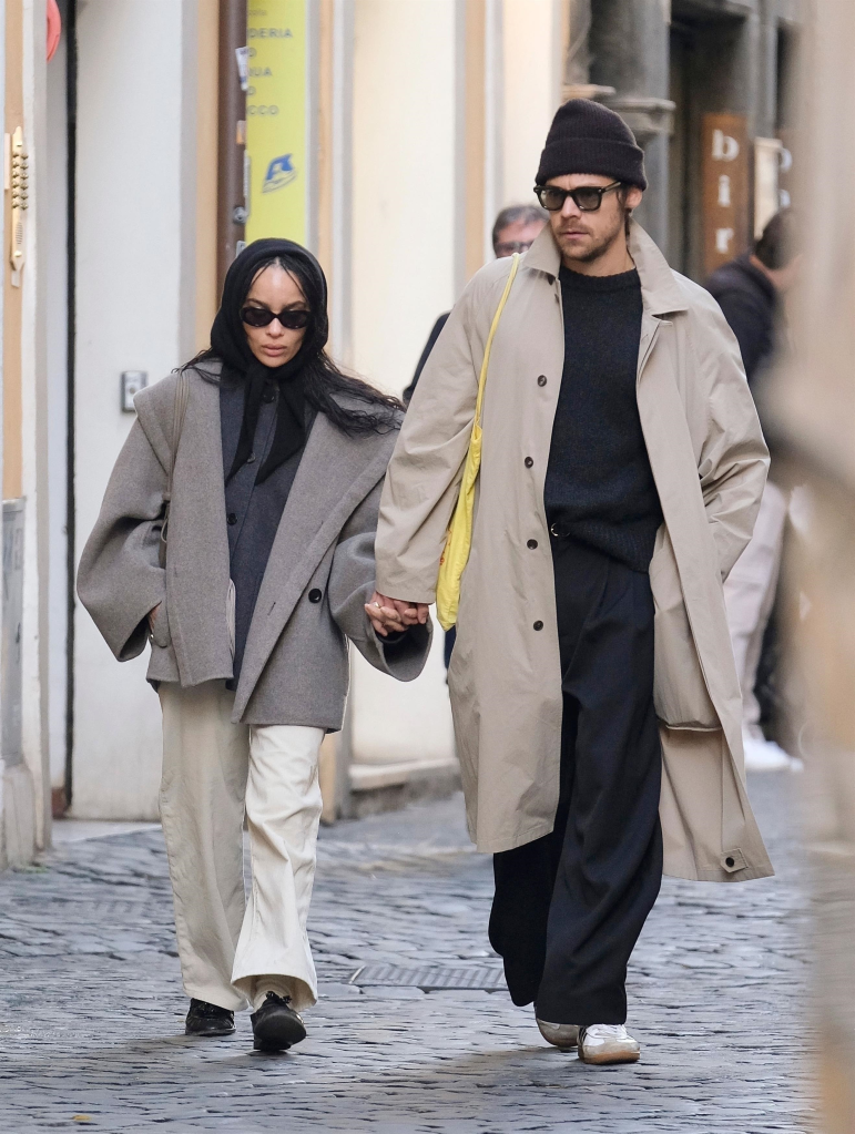 Harry Styles in a beige trench coat and Zoe Kravitz in a gray coat, holding hands while shopping in Rome.