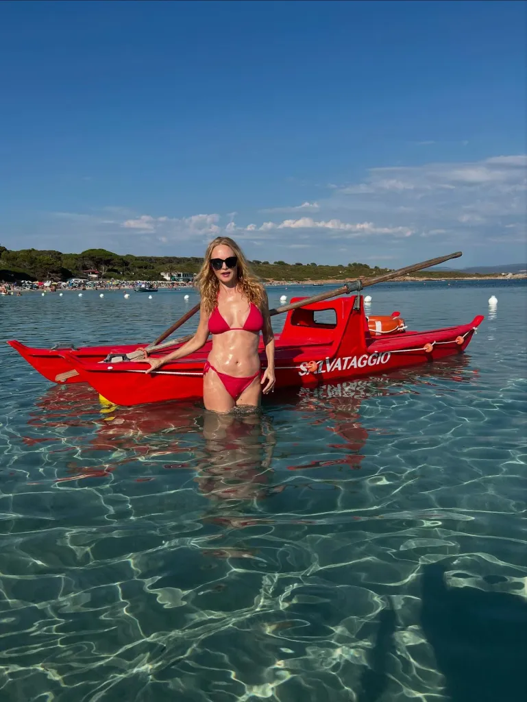 Heather Graham standing in clear water next to a red 