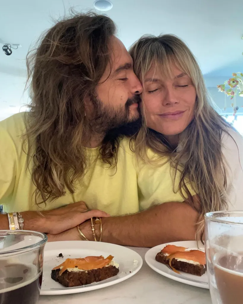 Heidi Klum and husband Tom Kaulitz cuddle at a table with plates of food and drinks.