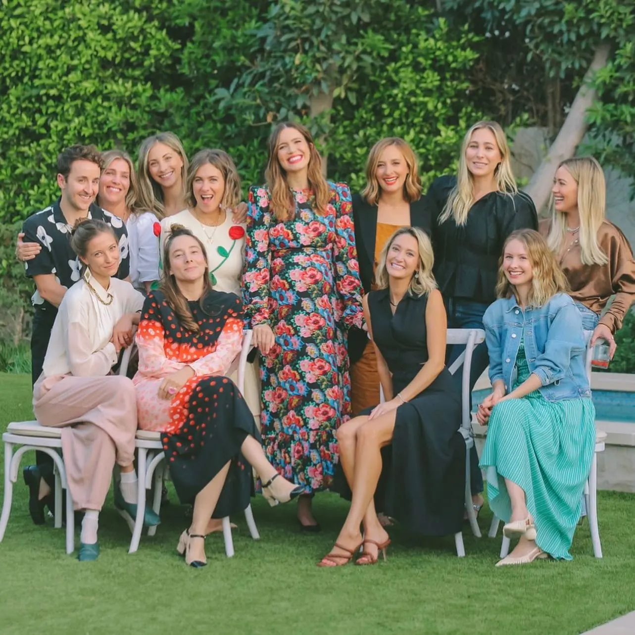 Hilary Duff with a group of friends, some seated and some standing, outdoors in a garden.
