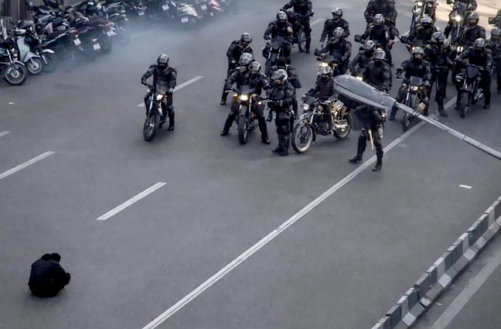 An unarmed protester sits in the road, facing a line of armed riot police on motorcycles during Iran protests on December 29, 2023.