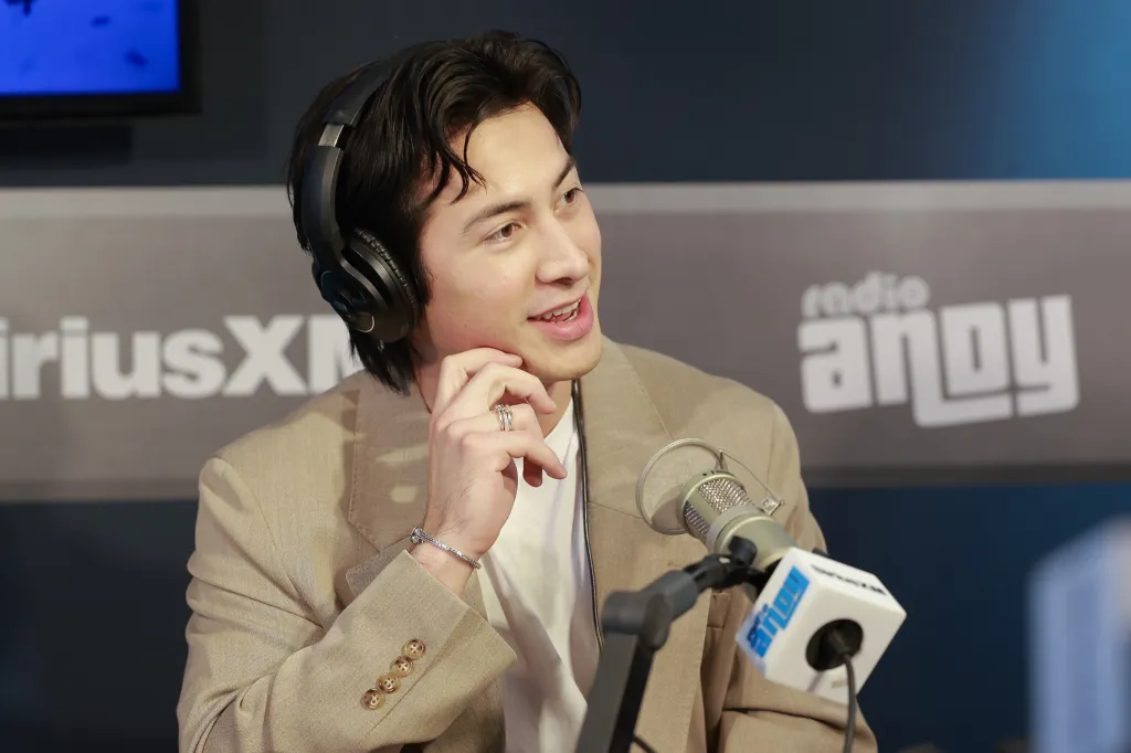 Hudson Williams wearing headphones and a tan suit, speaking into a microphone at SiriusXM Studios.