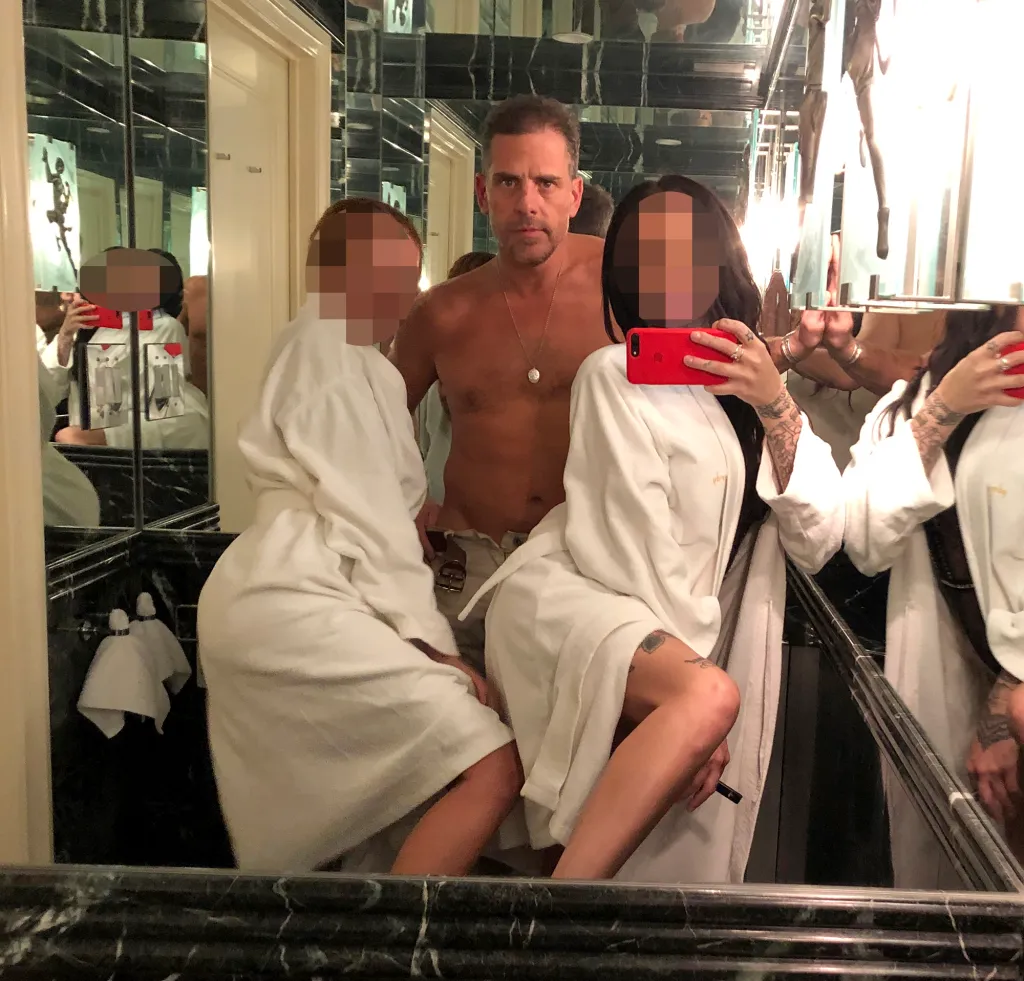 Hunter Biden posing with two blurred women in bathrobes in a mirrored room.