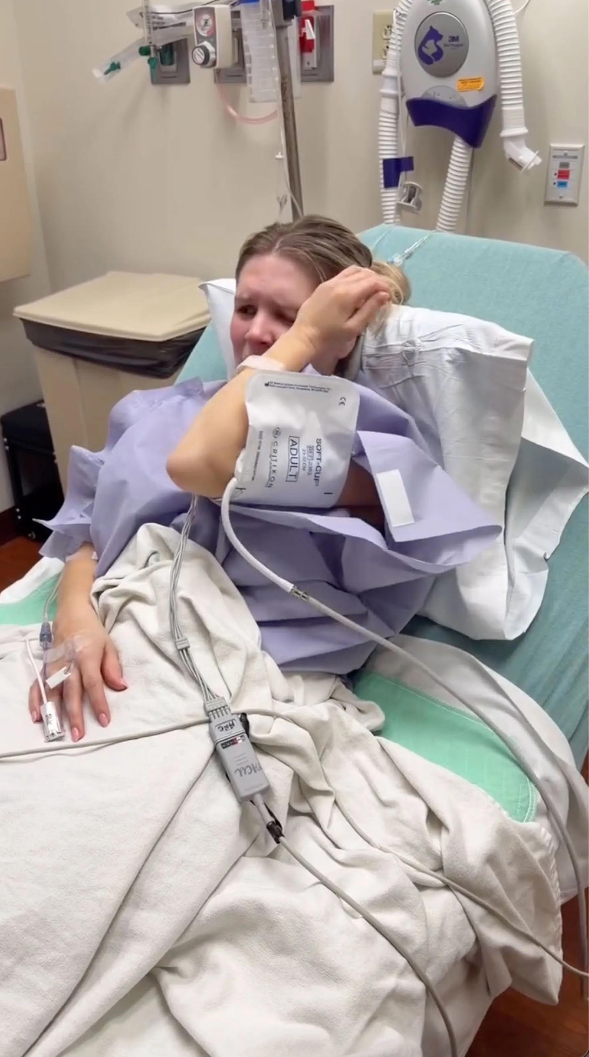 Katie Bates crying in a hospital bed with medical equipment attached to her.