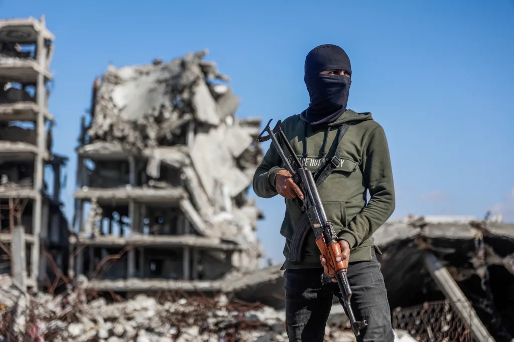 Hamas militant holding a rifle in front of a destroyed building in Jabalia refugee camp.