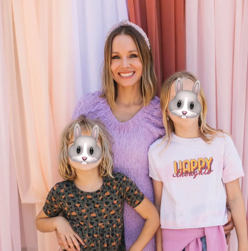 Kristen Bell posing with her two daughters whose faces are covered by bunny emojis.
