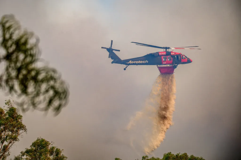 An Aerotech firefighting helicopter drops water over a fire.