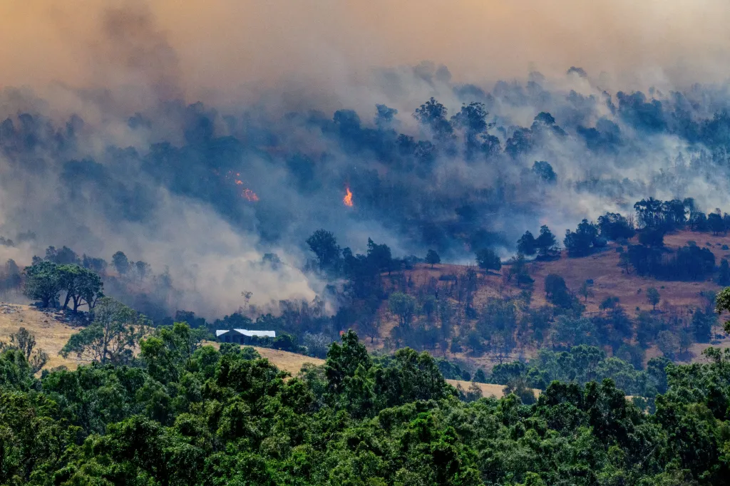 Smoke rises from a burning forest on a hillside behind a home near Longwood, Australia.