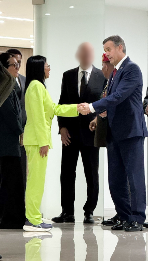 A woman in a neon green pantsuit shakes hands with a man in a navy suit.