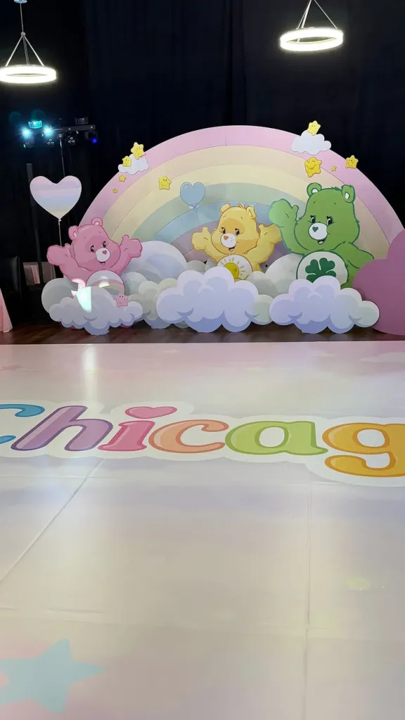 Care Bear-themed birthday party decoration with a rainbow backdrop, clouds, and cutout characters.