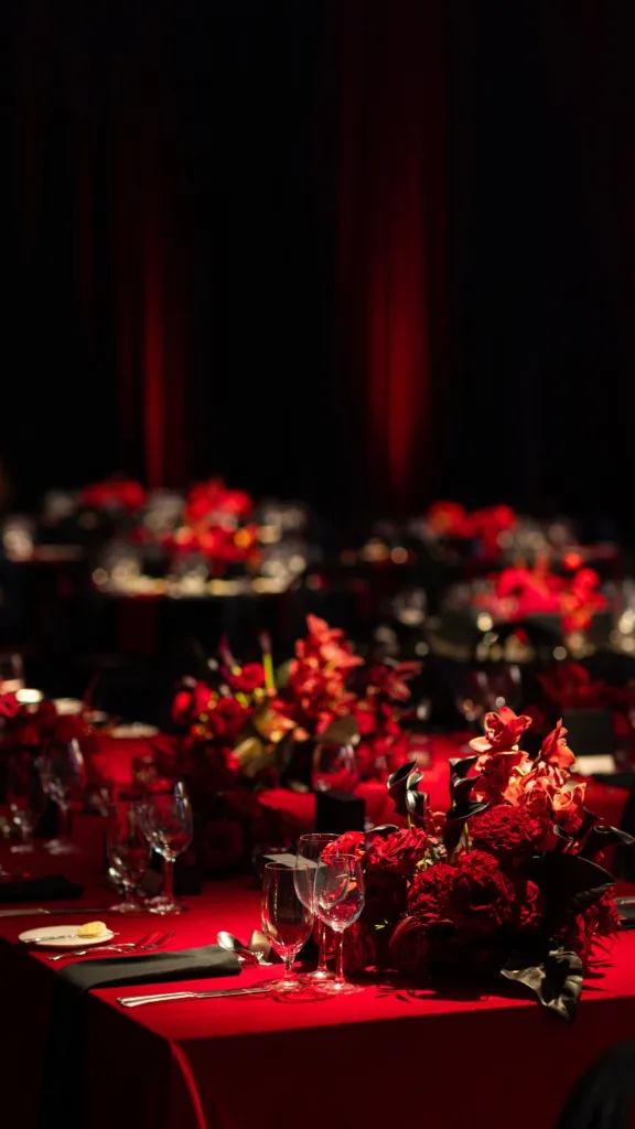 Red floral arrangements and place settings on a long red tablecloth.