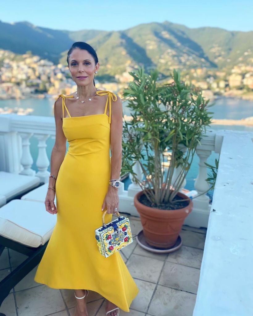 Bethenny Frankel in a yellow dress holding a floral patterned handbag.