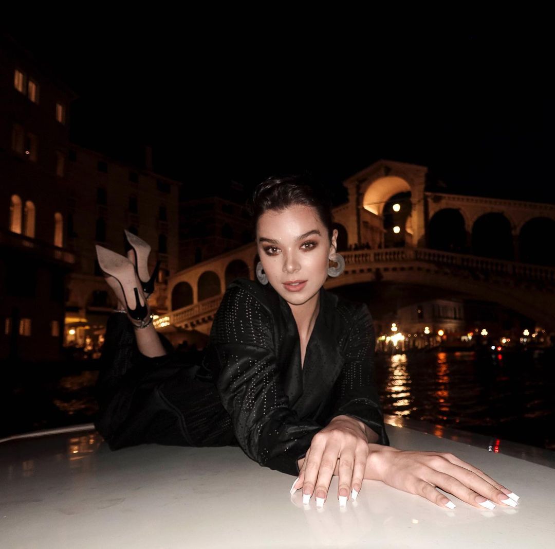 Hailee Steinfeld lying down at night with a bridge and canal in the background.