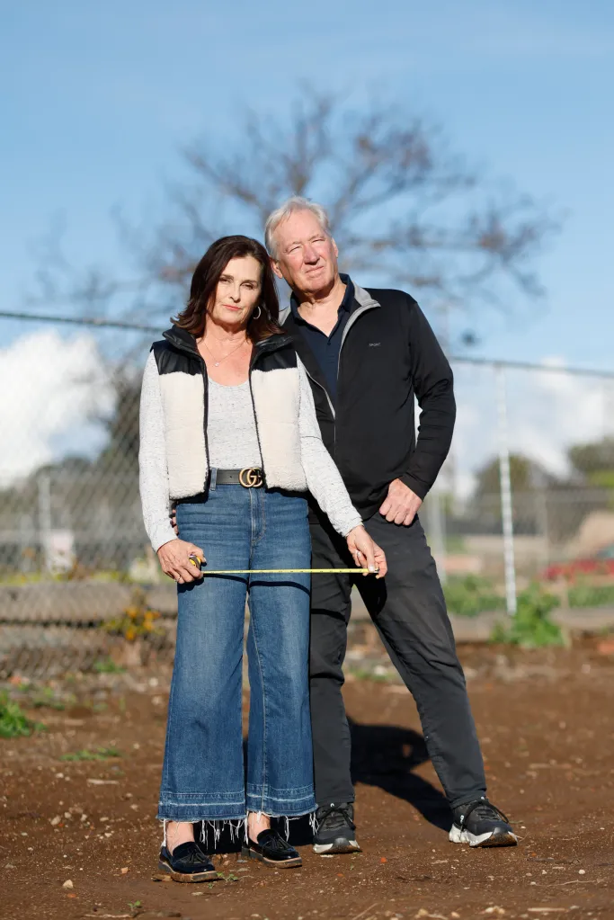 Kimberly Bloom and Martin McMahan hold a measuring tape on their property nearly a year after the Palisades fire.
