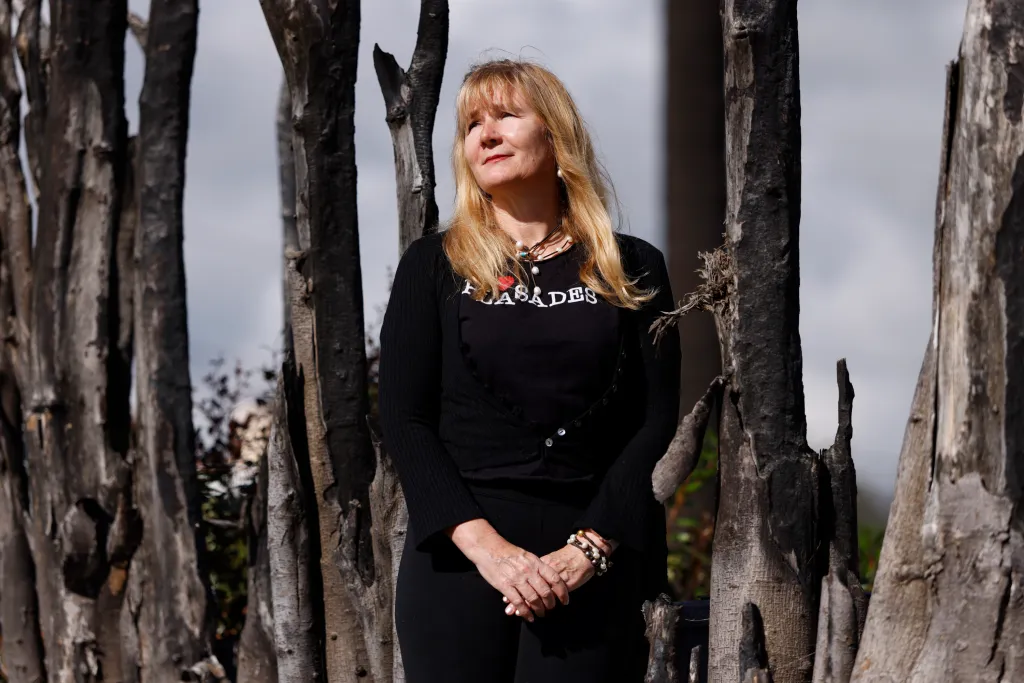 Sara Trepanier standing next to burnt trees on her property nearly a year after the Palisades fire.