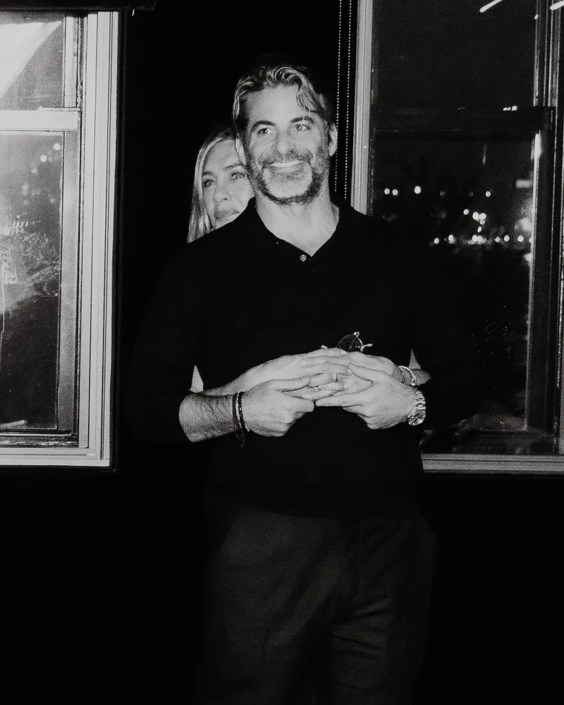 Black and white photo of Jennifer Aniston embracing Jim Curtis from behind, holding his hands.