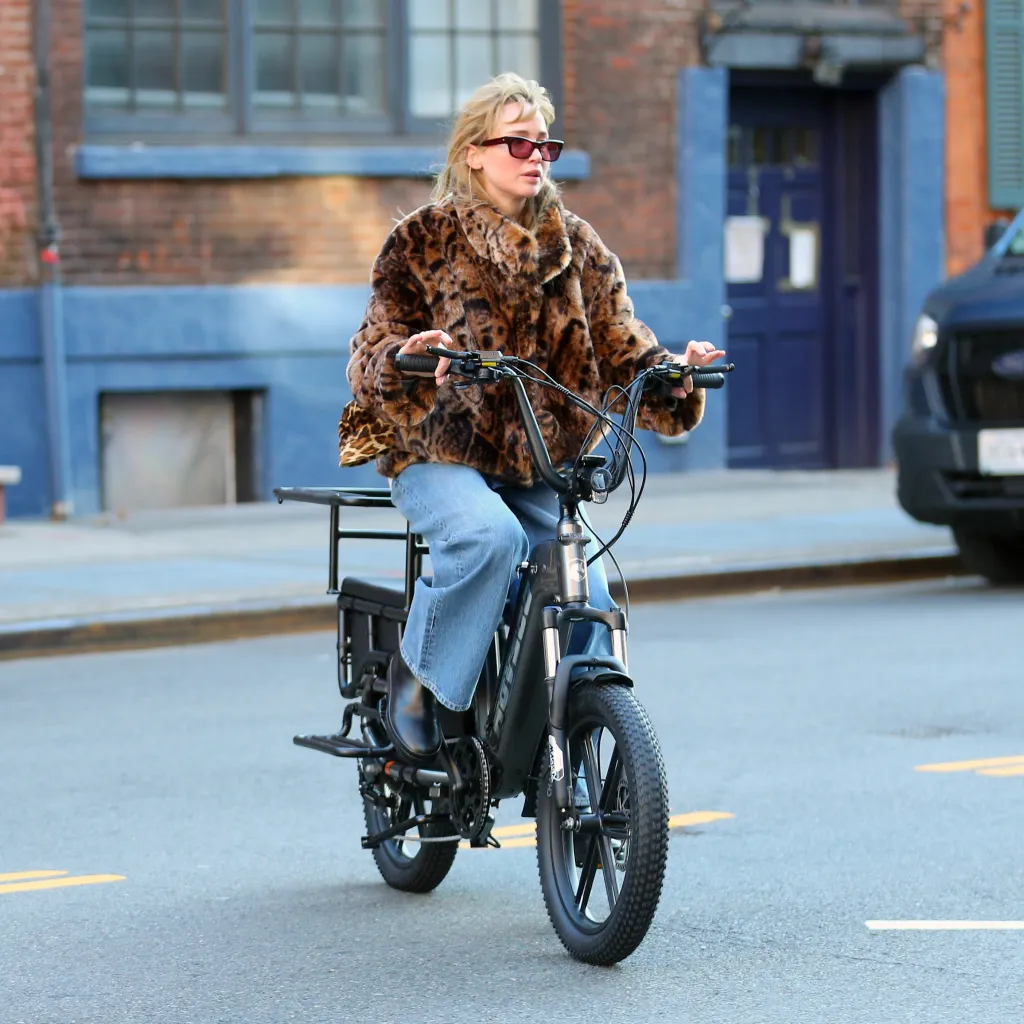 Jennifer Lawrence rides a Hovsco electric cargo bike wearing a faux leopard Jacquemus jacket and jeans.