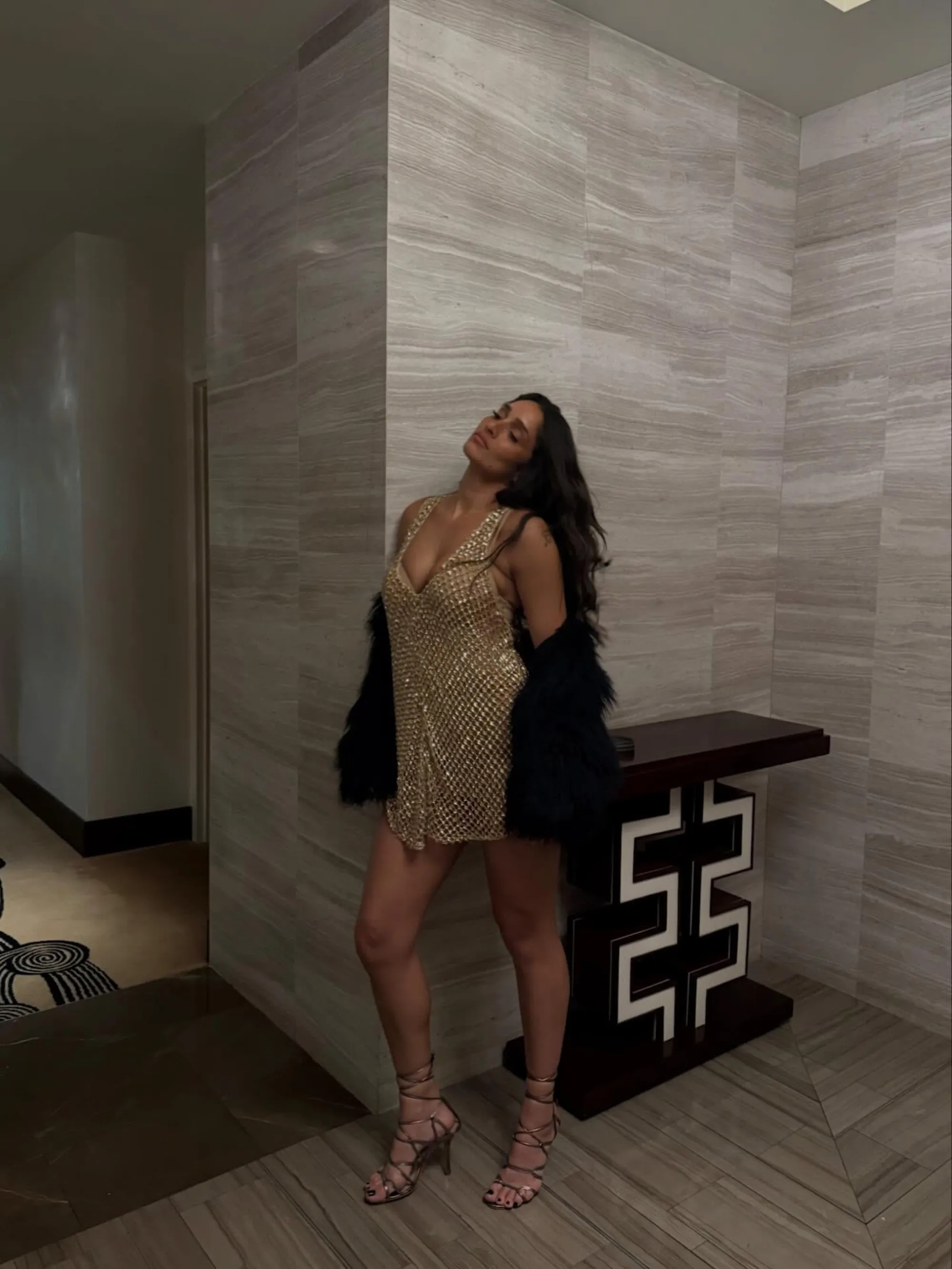 Tatiana Gabriela in a gold sequin dress, black fur coat, and lace-up heels.