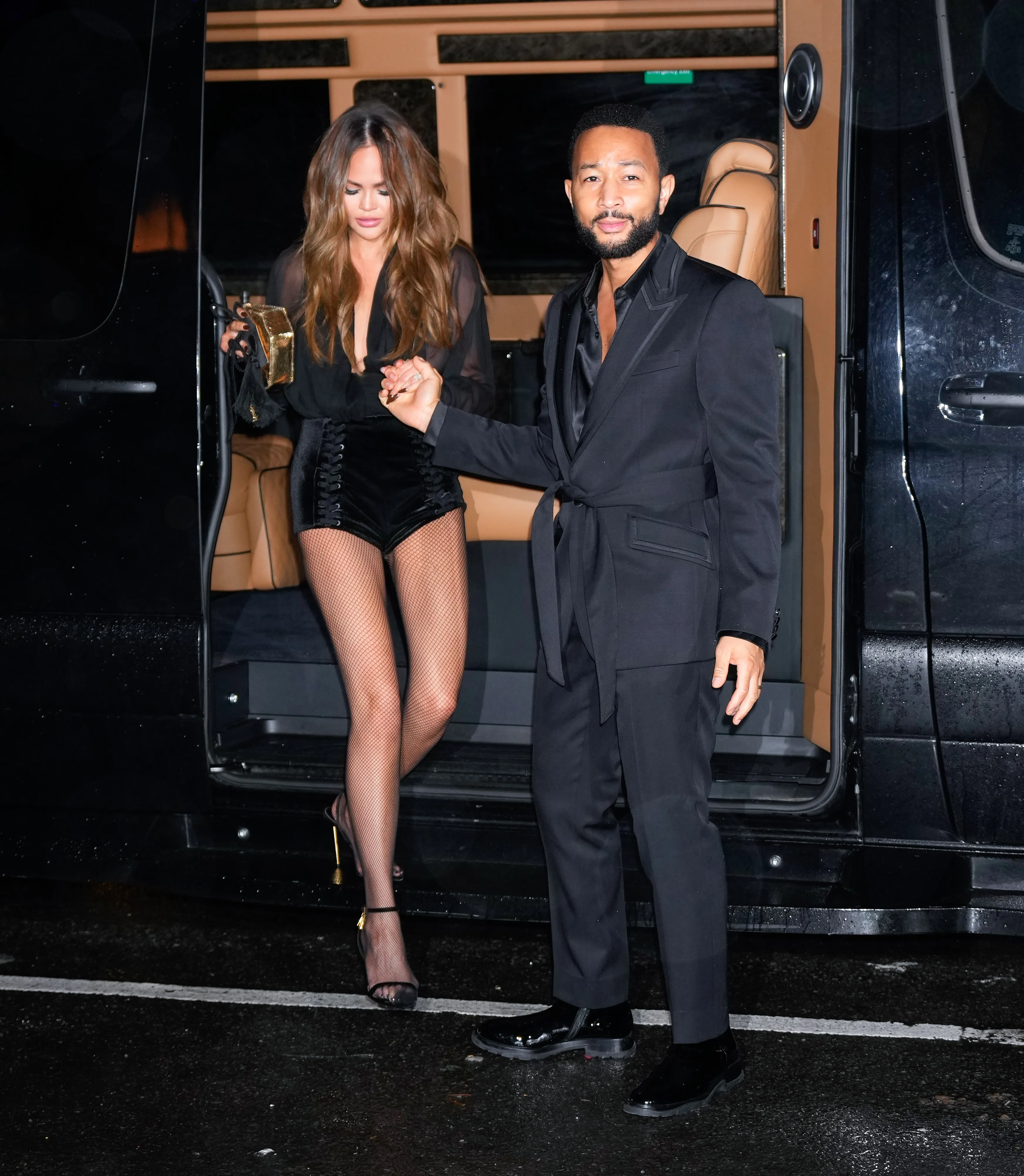 John Legend helps Chrissy Teigen out of a black van, holding her hand.