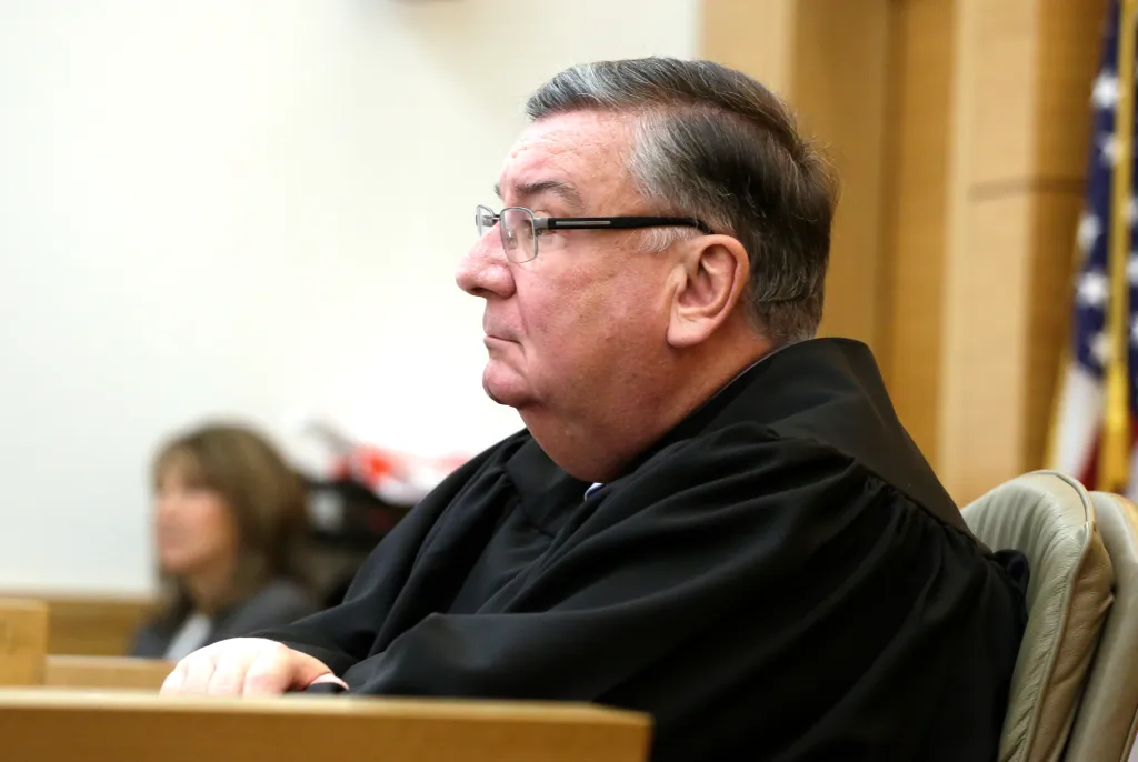 A judge in a black robe sits in a courtroom.