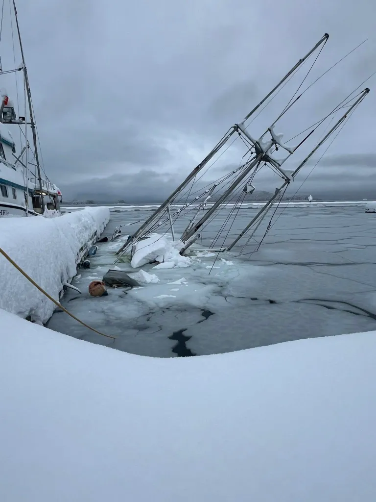 A sunken boat in a frozen harbor, with its masts angled into the icy water.