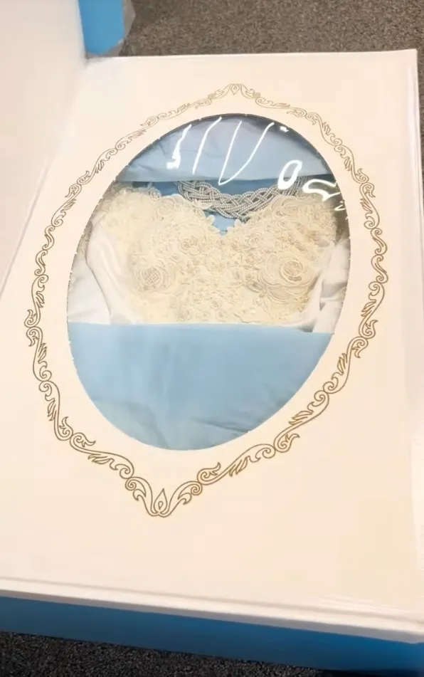 Vintage wedding dress in a decorative white box with a clear oval window.