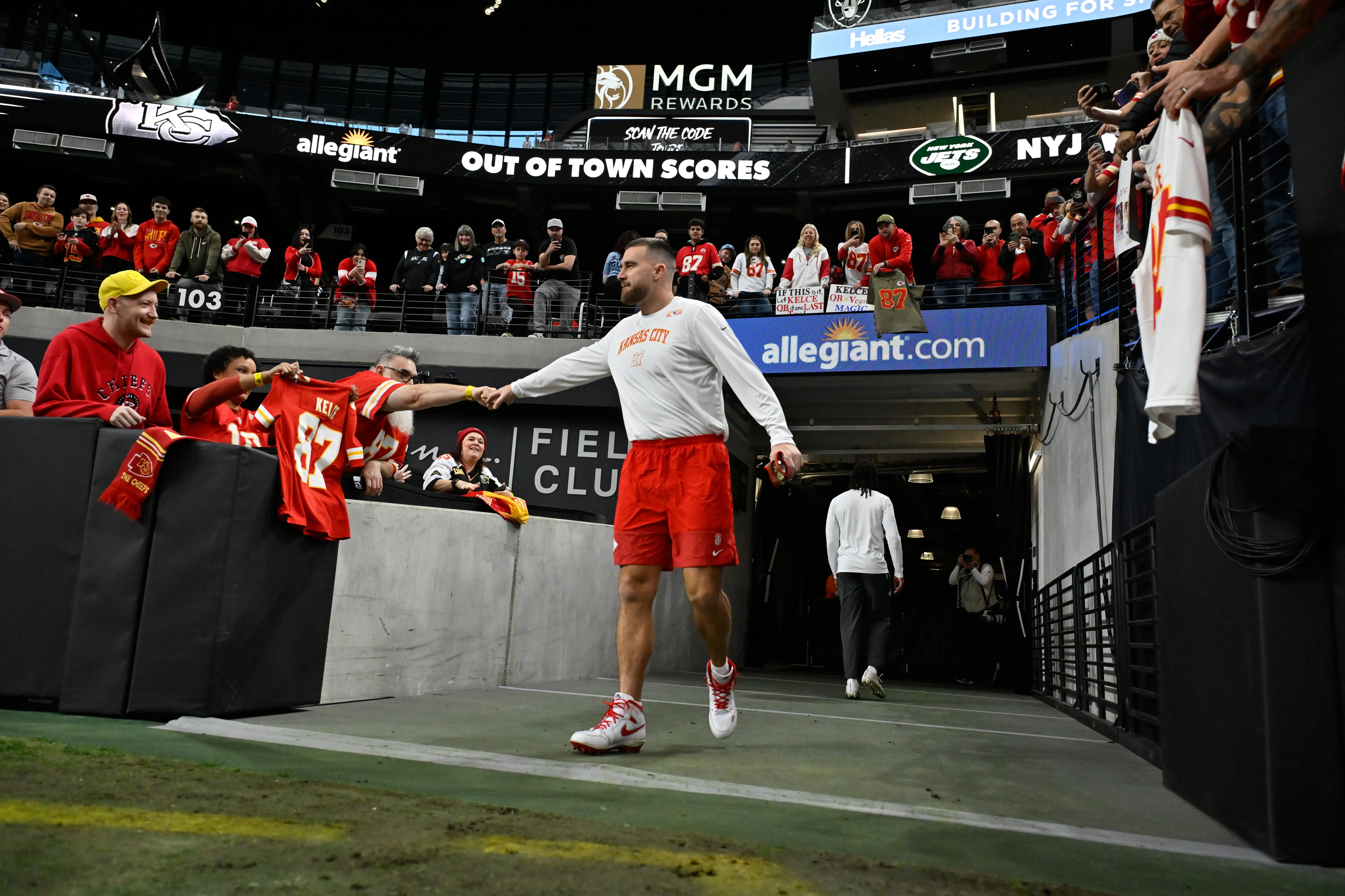 Kansas City Chiefs tight end Travis Kelce fist-bumps a fan holding a jersey on the sidelines.