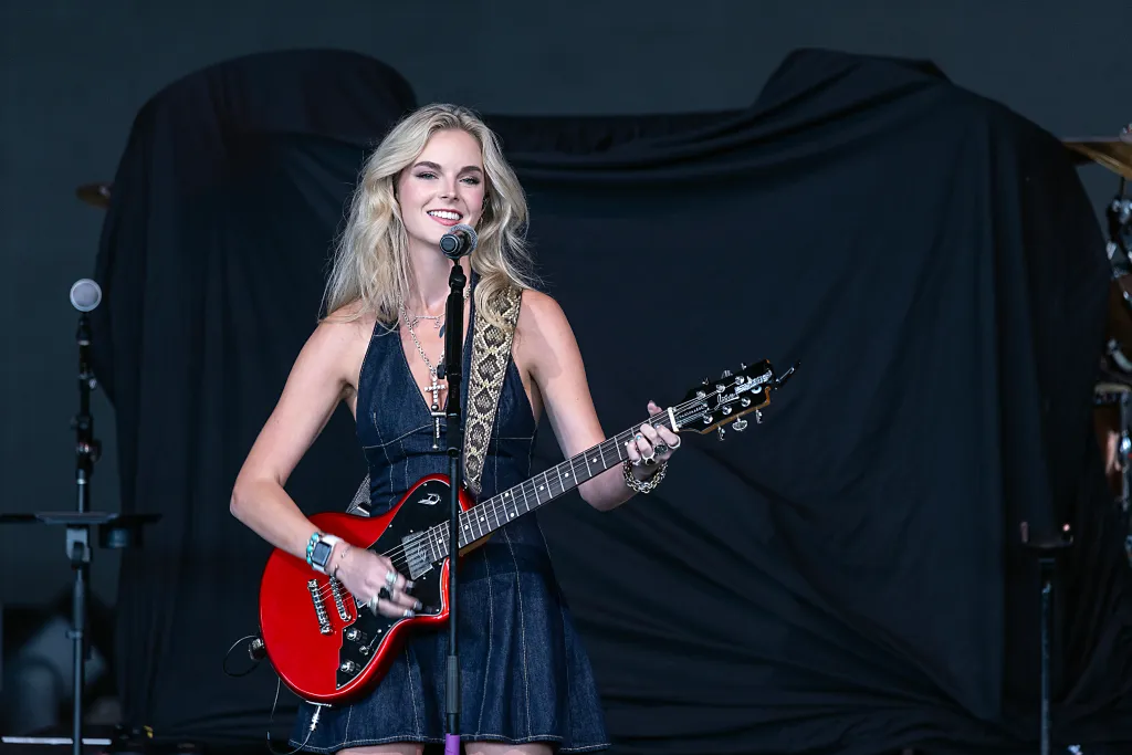Karley Scott Collins performing with a red electric guitar and singing into a microphone.