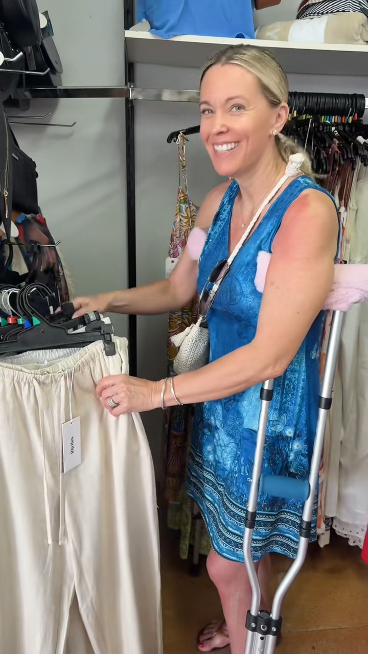 Kate Gosselin in a blue dress with crutches, smiling and looking at a pair of pants in a store.