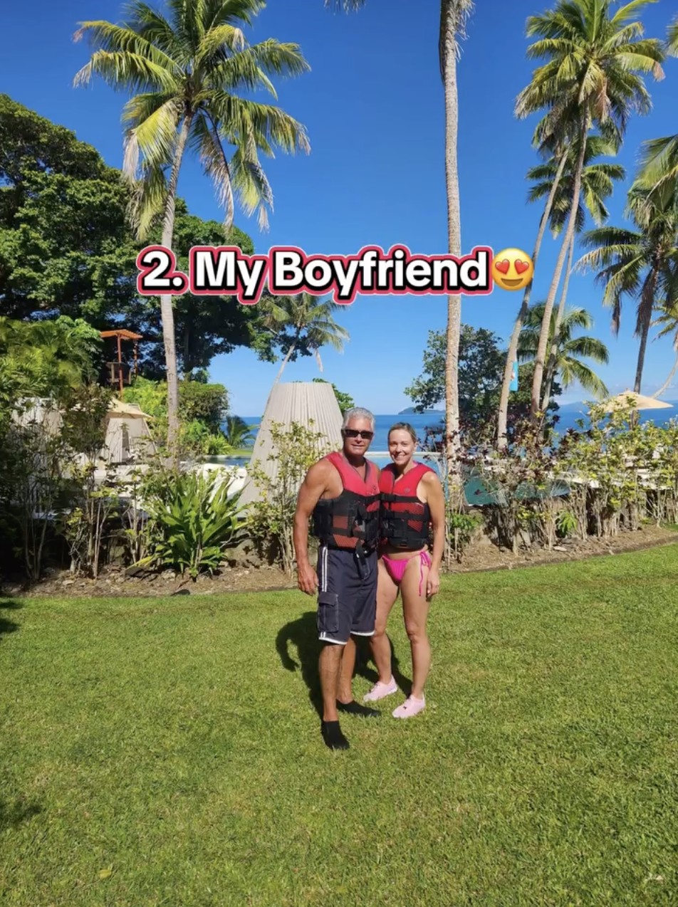 Kate Gosselin and Steve Neild in life jackets on a grassy lawn with palm trees and a body of water in the background.