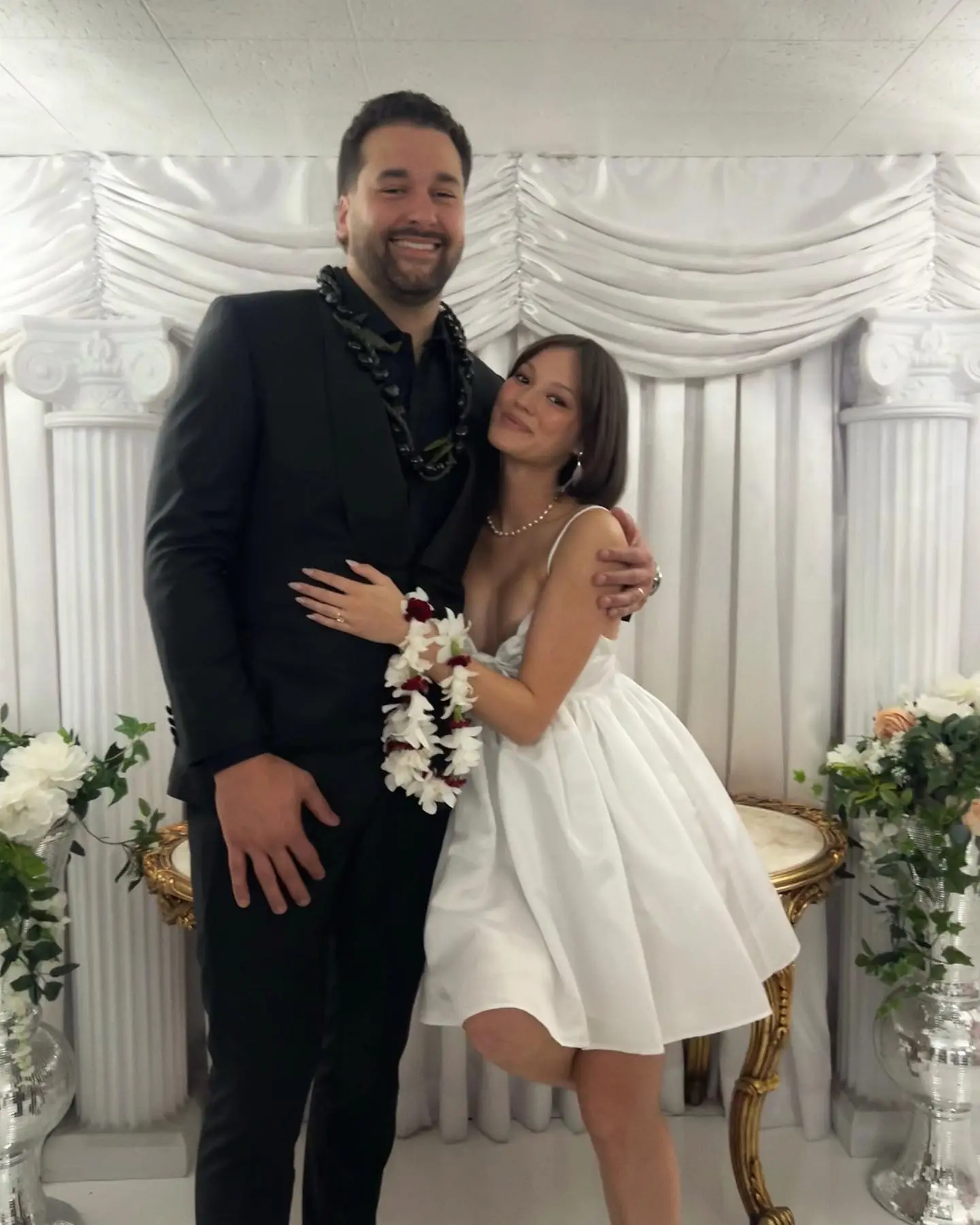 Keilani Asmus and Matt Kalil posing together, Kalil wearing a dark suit with a lei, and Asmus wearing a white dress and a lei bracelet.