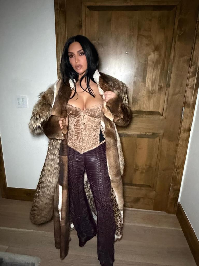 Kim Kardashian wearing a fur coat over a gold corset and maroon textured pants.