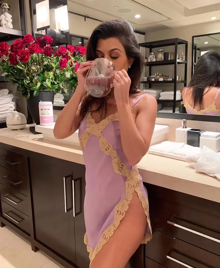 Kourtney Kardashian drinking from a glass mug while wearing a purple nightgown.