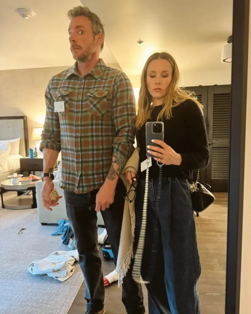 Kristen Bell taking a mirror selfie with Dax Shepard looking away in a hotel room.