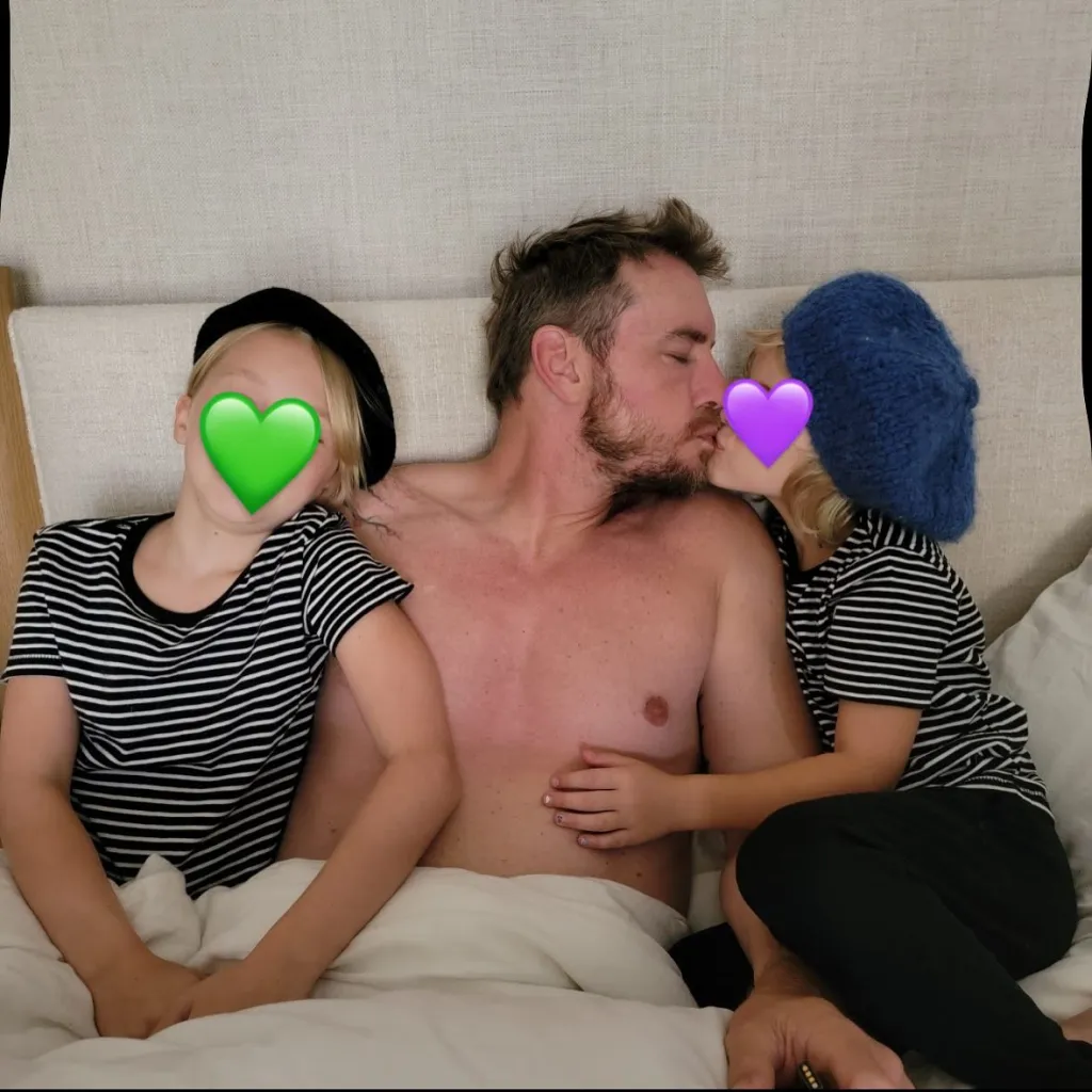 Dax Shepard with his two daughters in bed, one kissing him on the cheek.