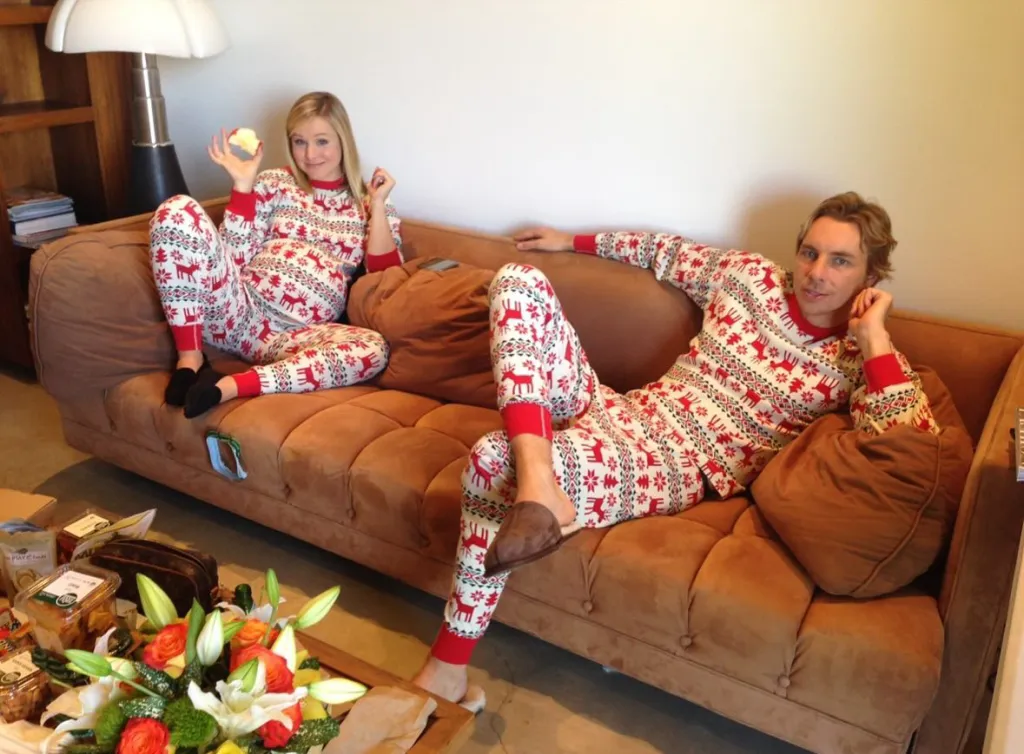 Kristen Bell and Dax Shepard in matching reindeer pajamas on a couch.