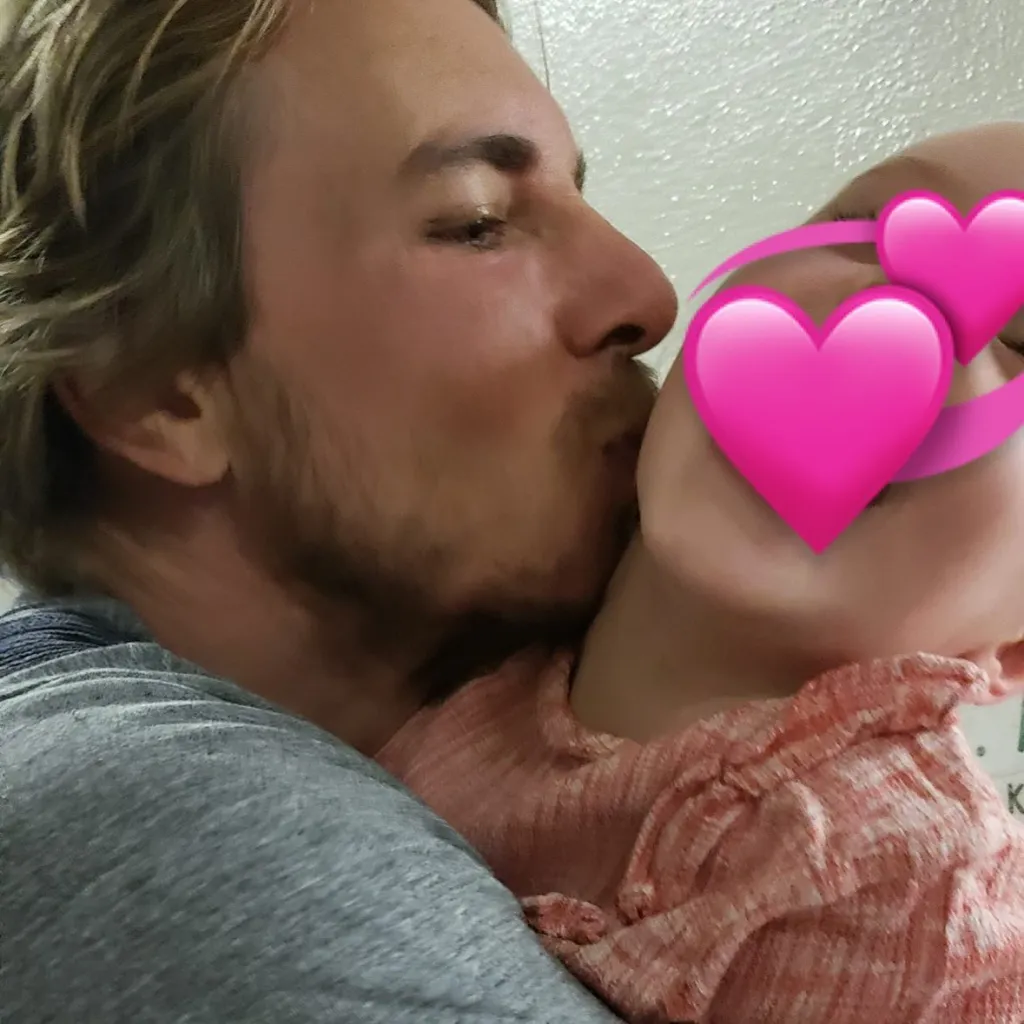 Dax Shepherd kissing one of his daughters, whose face is covered by pink heart emojis.