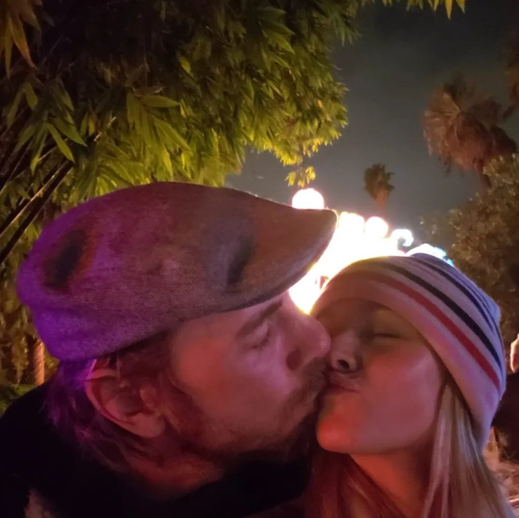 Kristen Bell kissing Dax Shepherd, both wearing hats.